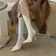 Blythe Pointed Leather Boots - seated side shot on model, cream - Miss Mosa By Akanksha
